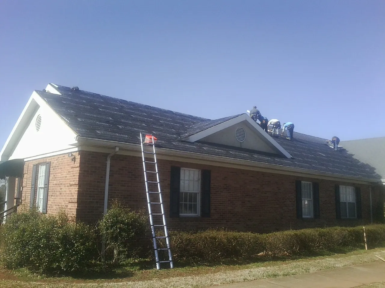 Crew tearing shingles off a brick ranch roof with a ladder set — Metal Roof Repair work by our crew in Brazoria