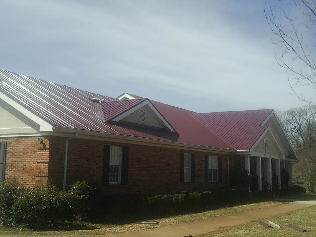 Red metal roof with gabled entries on a long brick building, from a Hail Damage Roof Repair job in Brazoria