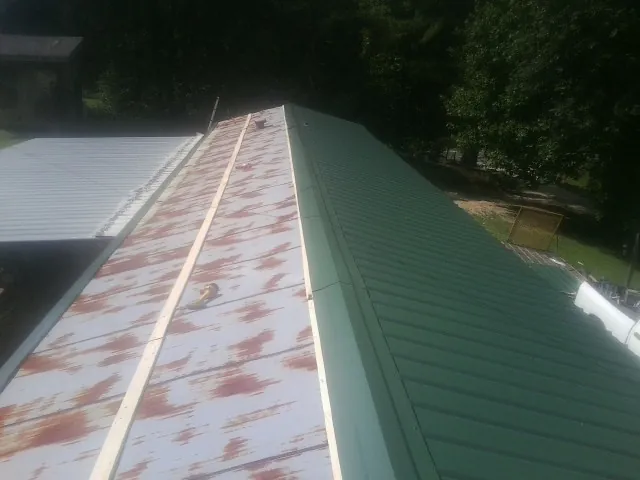 Old rusted panels beside newly installed green metal roofing — Wind Damage Roof Repair by Roofing Brothers in Brazoria