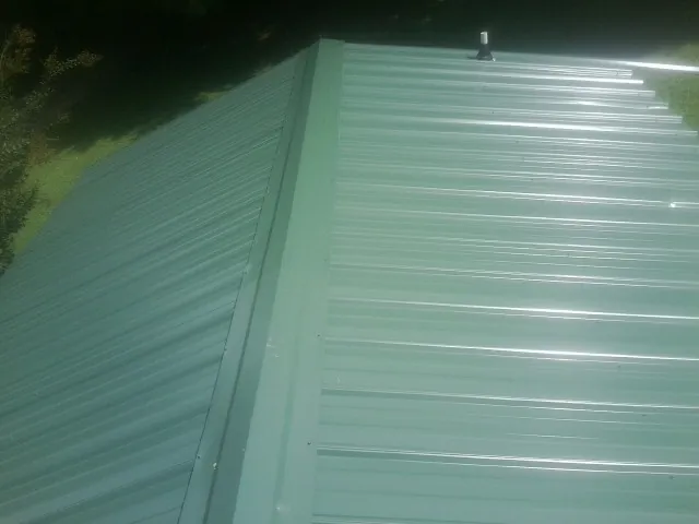 New green metal panels meeting at the ridge of a roof — Flat Roof Repair work by our crew in Brazoria