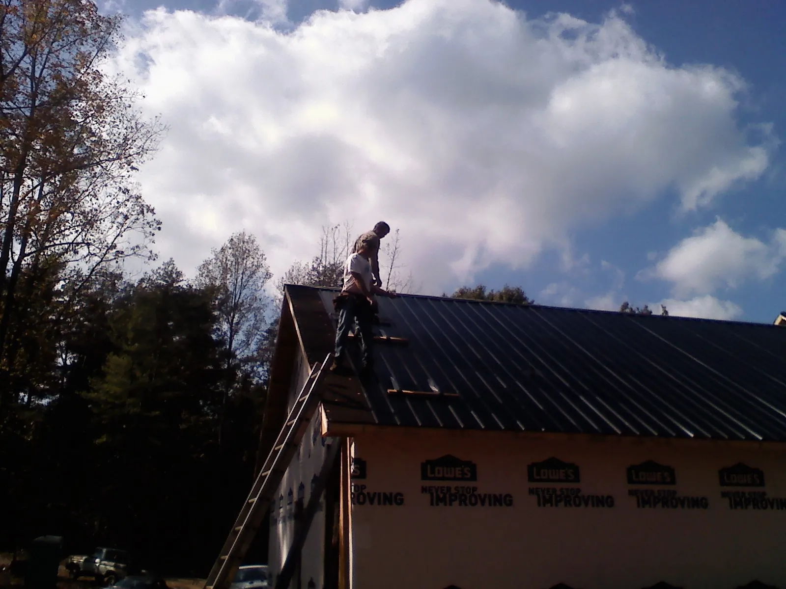 Roofer fastening dark metal panels high against a cloudy sky, from a Roof Inspection job in Brazoria