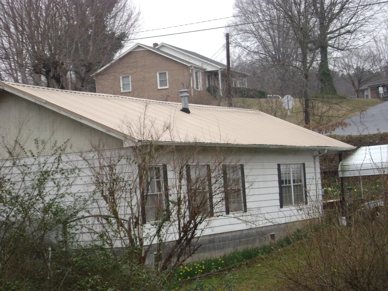 Tan metal roof on a white sided house set into a hillside — Commercial Roofing by Roofing Brothers in Brazoria