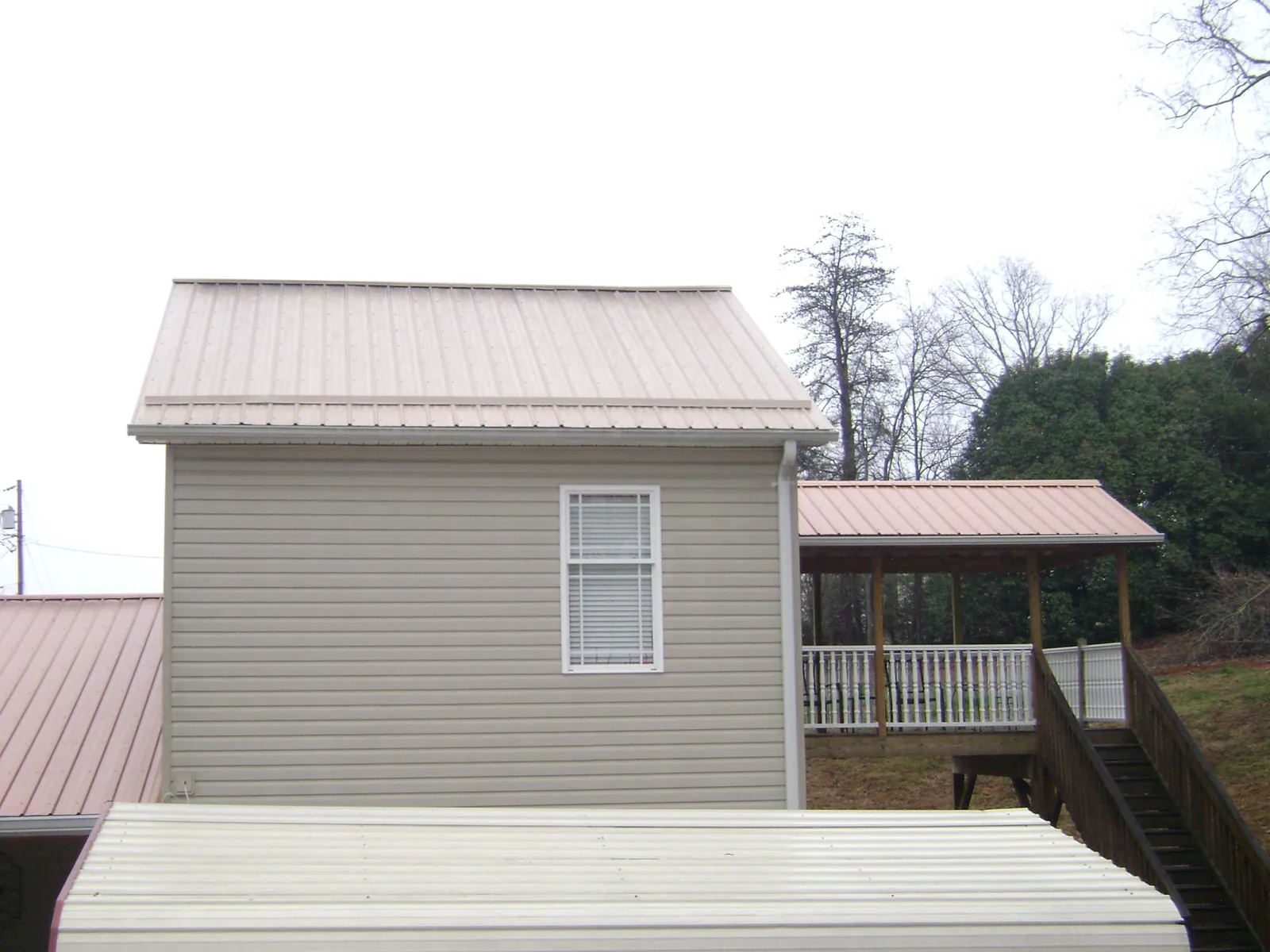Tan metal roofs on a two story addition and attached porch, from a Roof Replacement job in Brazoria